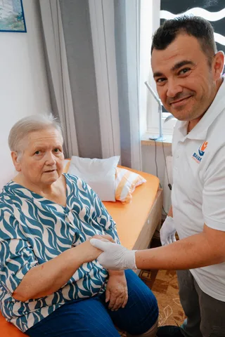 Pflegekraft von Bavaria Vitalpflegedienst begrüßt eine Seniorin per Handschlag beim Hausbesuch — wir versorgen Maxvorstadt in München