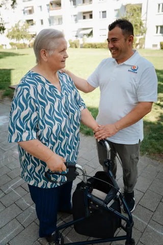 Pflegekraft von Bavaria Vitalpflegedienst begrüßt eine Seniorin mit Rollator im Freien — wir versorgen Ludwigsvorstadt-Isarvorstadt in München