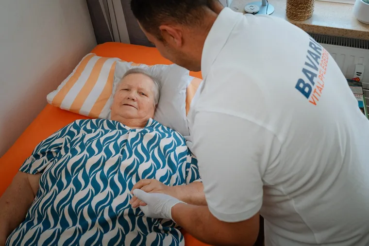 Pflegekraft von Bavaria Vitalpflegedienst lagert eine Patientin im Pflegebett um