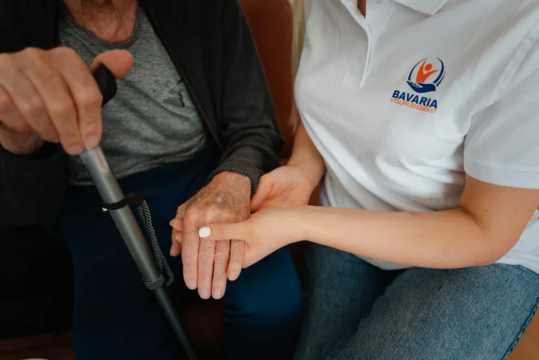 Pflegekraft von Bavaria Vitalpflegedienst reicht einem Senior die gestellte Tablette