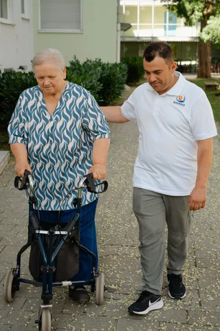 Pflegekraft von Bavaria Vitalpflegedienst begleitet eine Seniorin mit Rollator ins Freie — wir versorgen Neuhausen-Nymphenburg in München