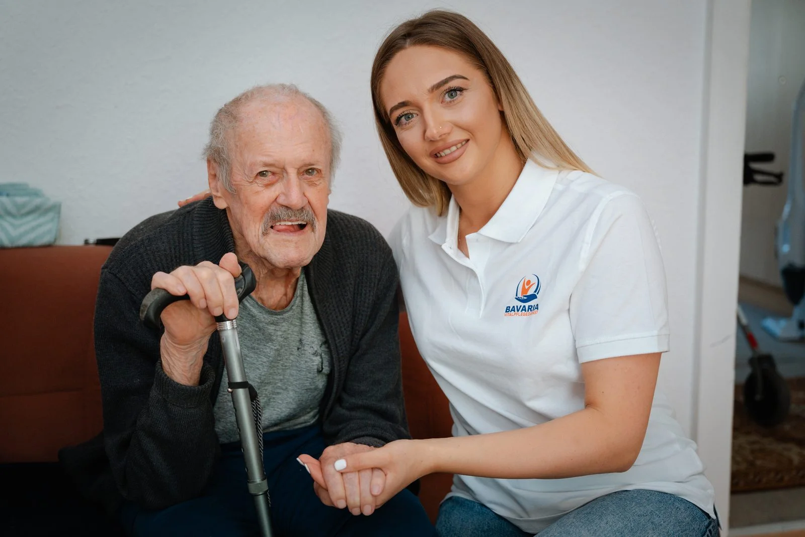 Pflegerin von Bavaria Vitalpflegedienst sitzt neben einem Senior und betreut ihn zu Hause