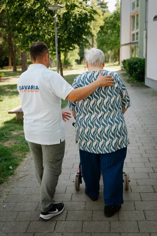 Pflegekraft von Bavaria Vitalpflegedienst stützt eine Seniorin beim Gehen im Freien — wir versorgen Pasing-Obermenzing in München