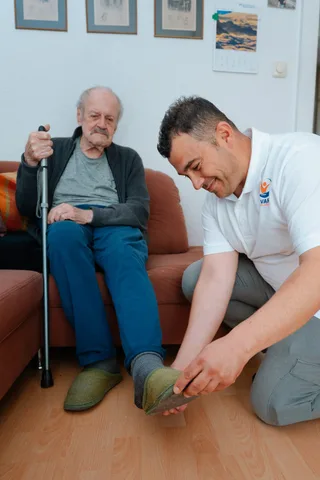 Pflegekraft von Bavaria Vitalpflegedienst hilft einem Senior beim Anziehen der Strümpfe — wir versorgen Milbertshofen-Am Hart in München